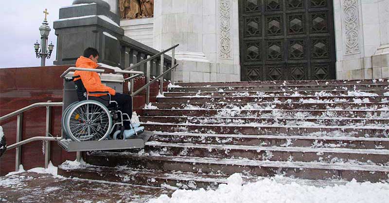Treppenplattformlift hebt Rollstuhl über die Freitreppe einer winterlichen Kirche