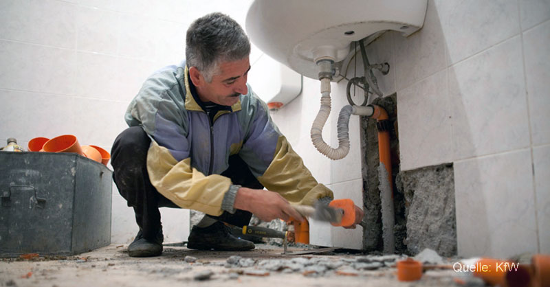 Handwerker verlegt eine Wasserleitung in der Wand unter einem Waschbecken